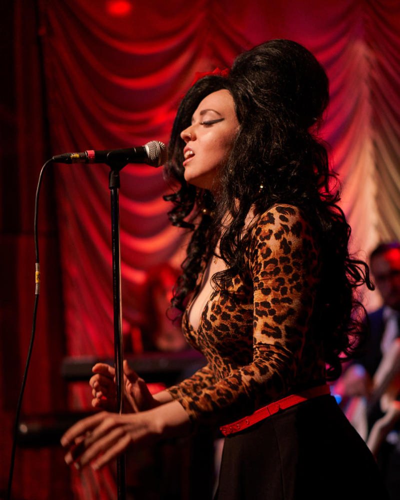 Alana Nabors as Amy Winehouse at the microphone, beehive and leopard print, in red stage light