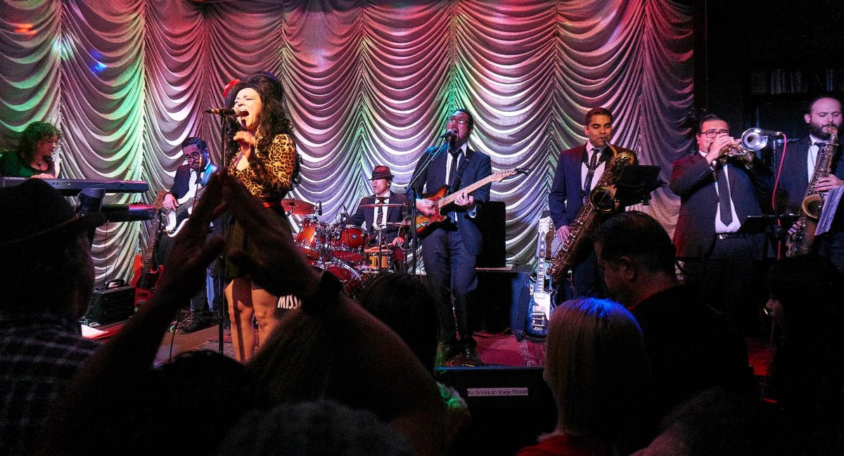 The full ten-piece band on stage seen from the crowd, horn section on the right